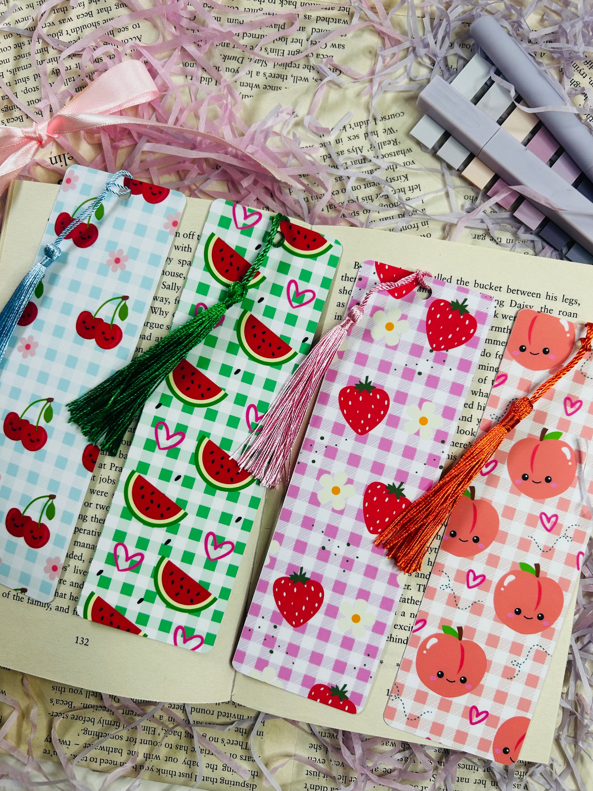 Set of colorful gingham bookmarks with fruit illustrations including cherries, strawberries, and citrus, placed on an open book.