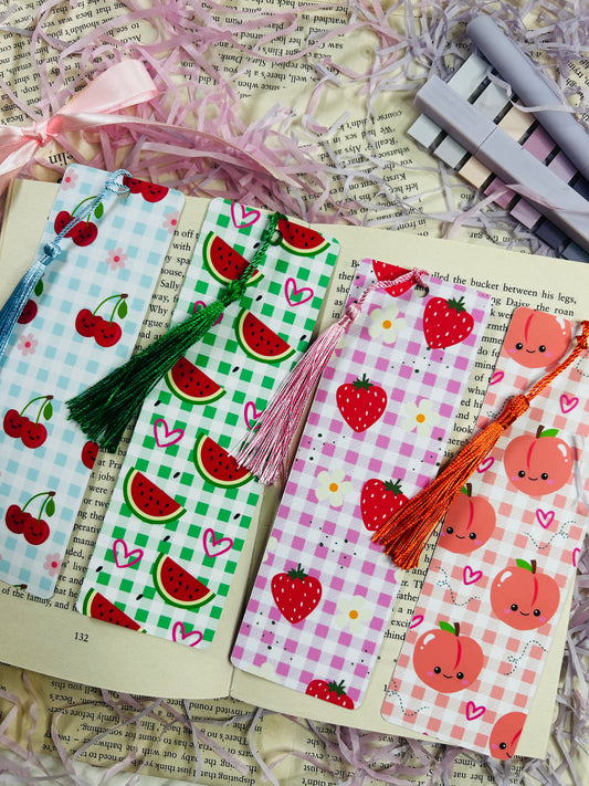 Set of colorful gingham bookmarks with fruit illustrations including cherries, strawberries, and citrus, placed on an open book.