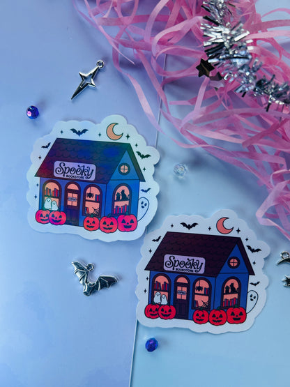 Two Halloween-themed stickers of a haunted house with pumpkins on a light blue background with decorative ribbons.
