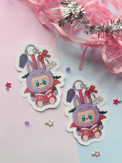 Two cute character stickers with keychains on a pink and white background.