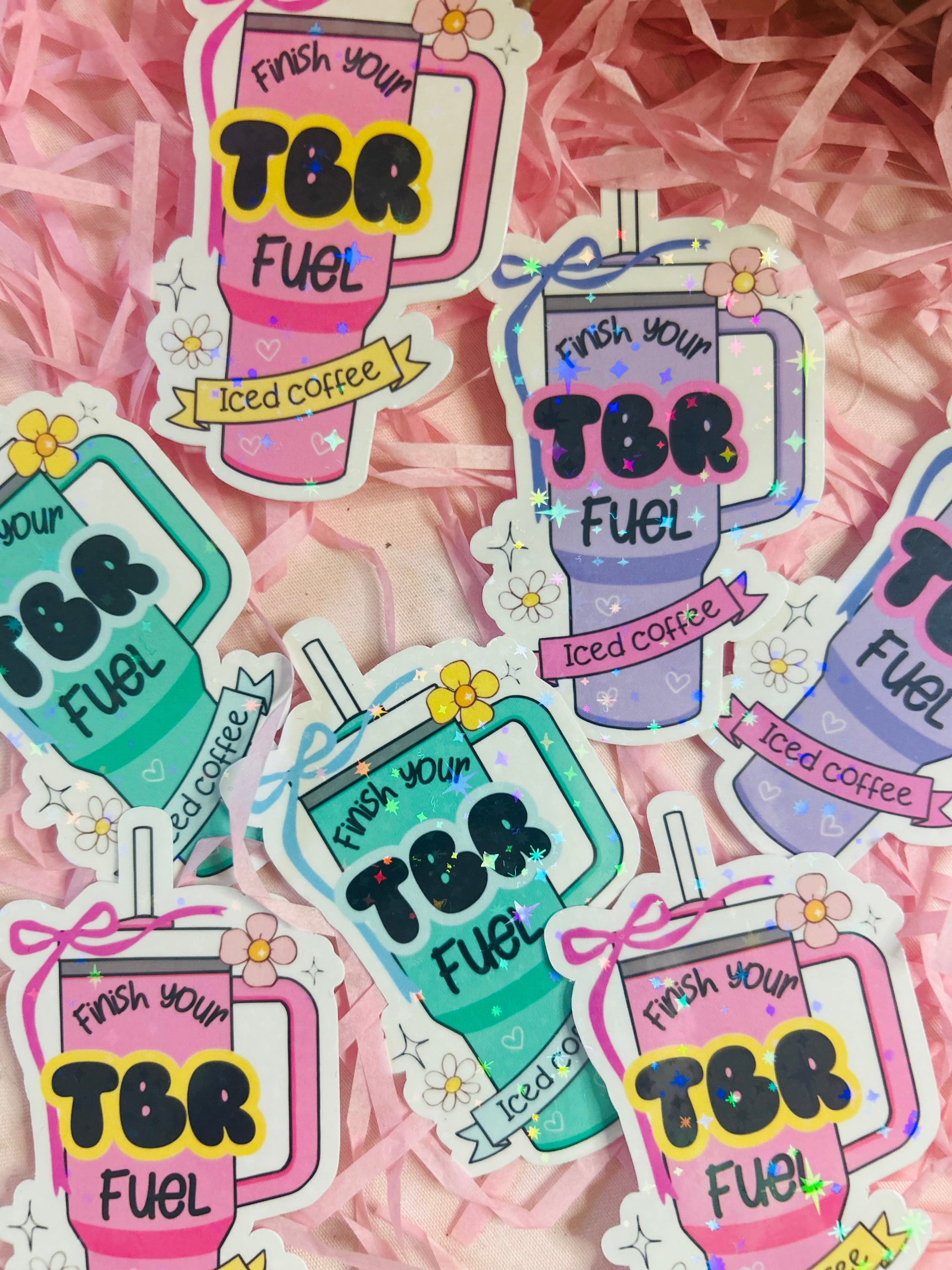 Pastel iced coffee bookish vinyl stickers with "Finish Your TBR Fuel" text, surrounded by pink shredded paper and decorative beads – perfect for readers and book lovers.
