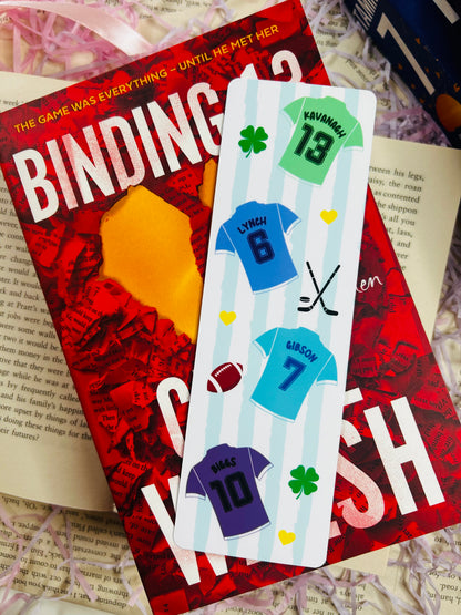 Bookmark with sports jersey designs labelled Kavanagh, Lynch, Gibson, and Biggs, laid over Binding 13 book.