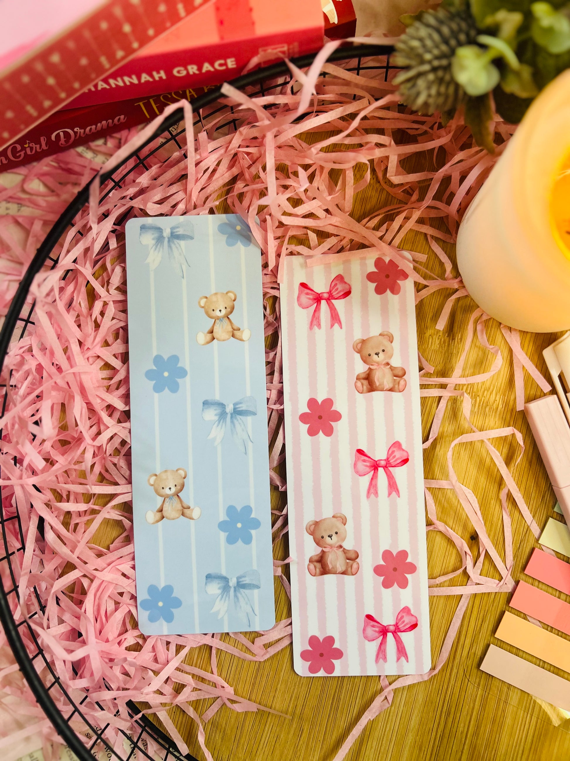 A set of two teddy bear-themed bookmarks, one in pink and one in blue, featuring soft pastel stripes, bows, and floral accents.