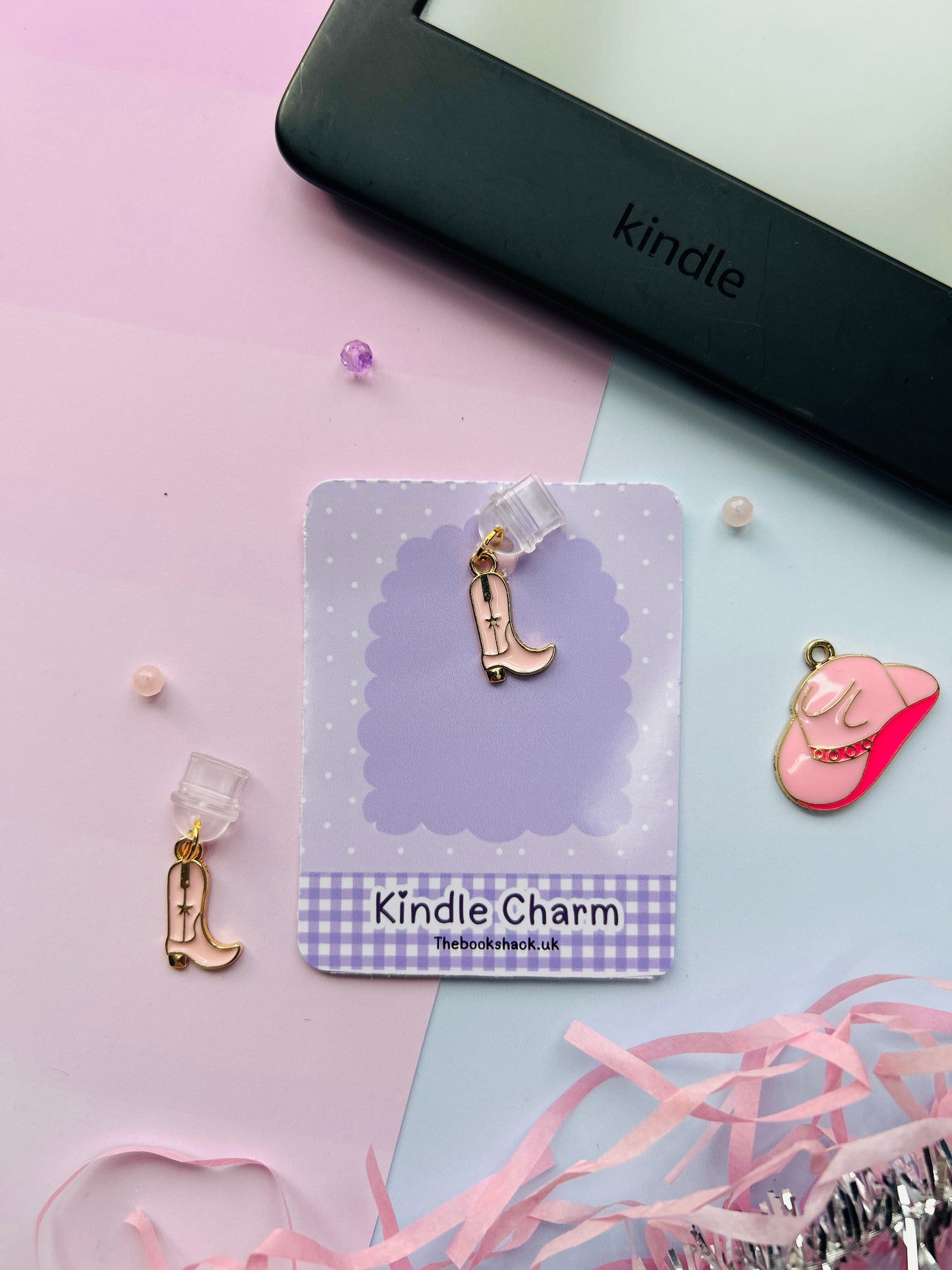 Pink cowboy boot Kindle charm attached to a clear plastic Type-C dust plug, shown with backing card and holographic packaging, plus optional white letter charm.