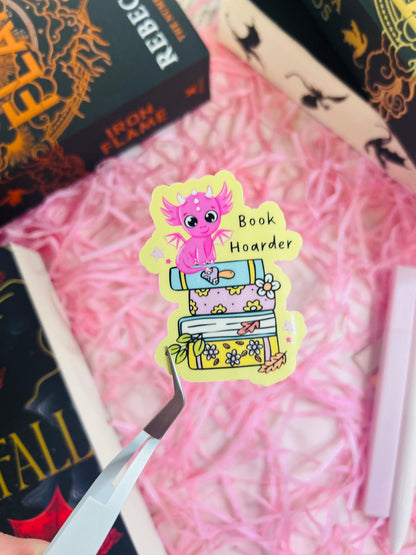 Close-up of a vibrant yellow 'Book Hoarder' dragon sticker featuring a pink baby dragon perched on a stack of pastel-coloured books