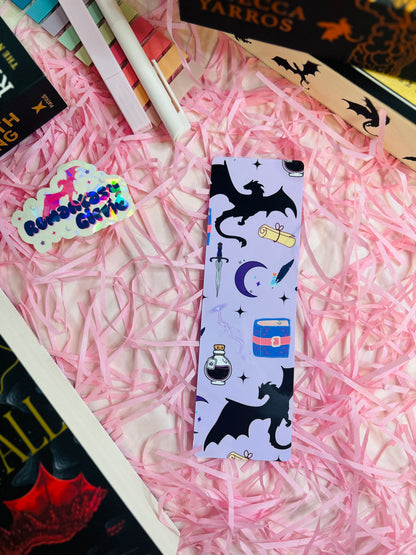 Fantasy-inspired bookmark with a light purple background, featuring a black dragon silhouette, mystical potion bottle, sword, scroll, moon, and stars