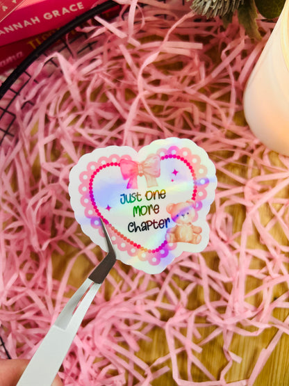 pink holographic sticker, with a love heart and teddy bear, featuring the quote 'just one more chapter'