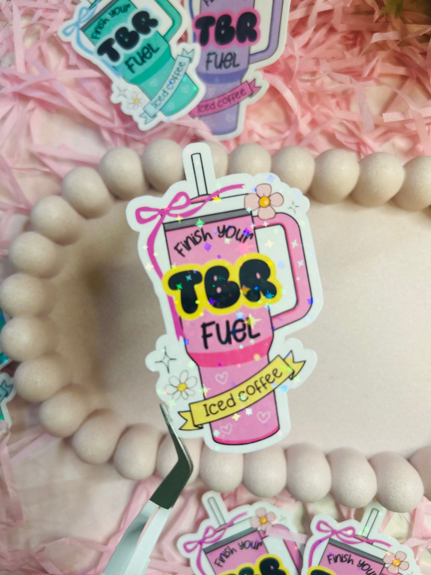 Pastel iced coffee bookish vinyl stickers with "Finish Your TBR Fuel" text, surrounded by pink shredded paper and decorative beads – perfect for readers and book lovers.