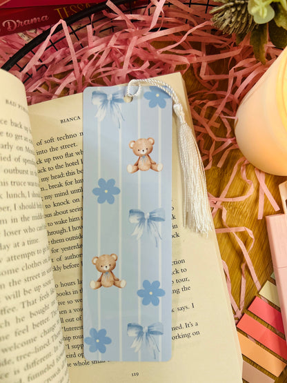 A blue teddy bear-themed bookmarks with pastel vertical stripes, delicate bows, and floral accents. Featuring a white tassel.
