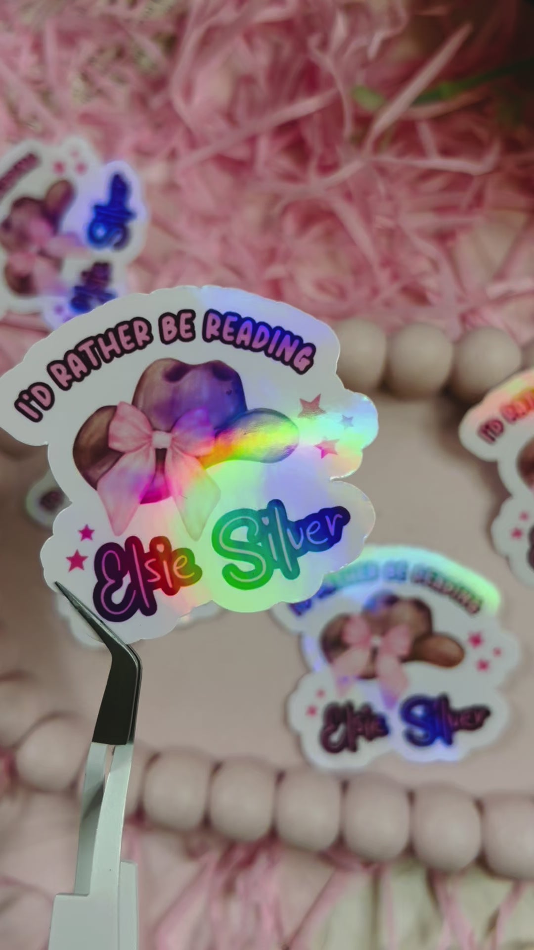 Holographic sticker with a pink-bowed cowboy hat and text reading "I'd Rather Be Reading Elsie Silver" on a bookish background with pink shredded paper