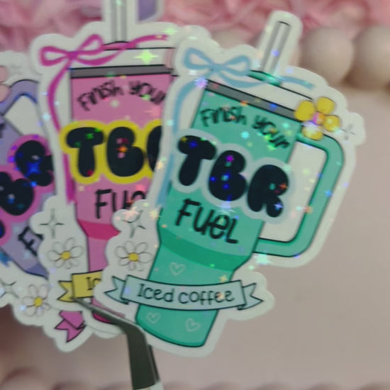 Pastel iced coffee bookish vinyl stickers with "Finish Your TBR Fuel" text, surrounded by pink shredded paper and decorative beads – perfect for readers and book lovers.
