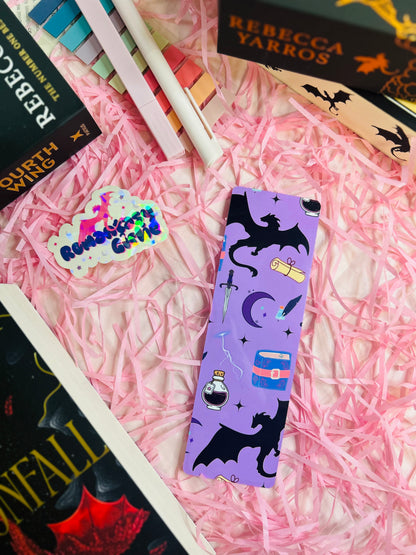 Purple fantasy-themed bookmark featuring a black dragon silhouette, potion bottle, sword, scroll, and celestial elements