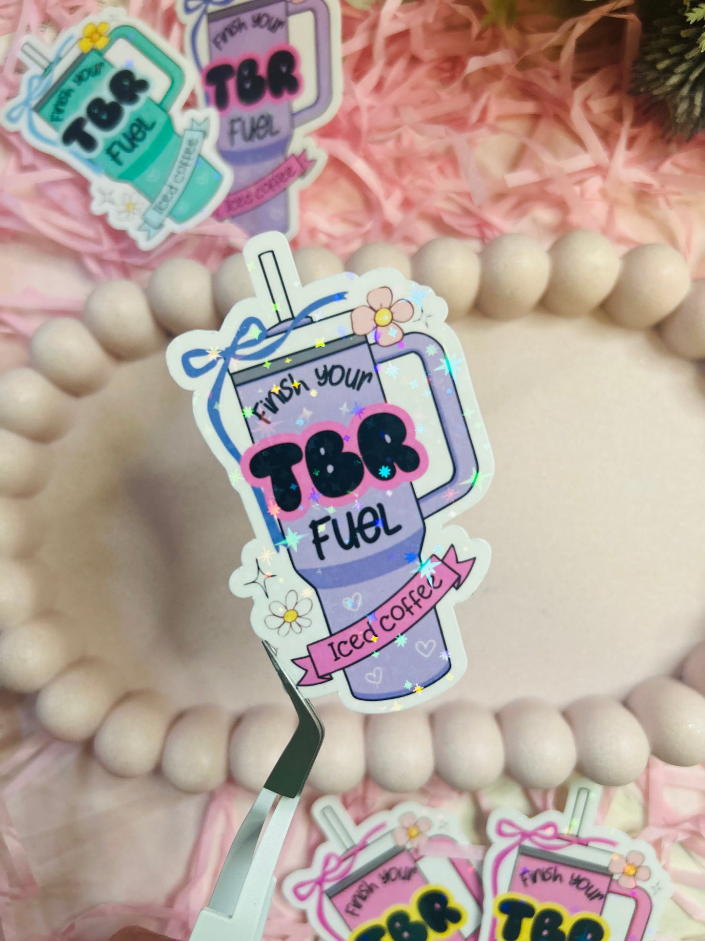 Pastel iced coffee bookish vinyl stickers with "Finish Your TBR Fuel" text, surrounded by pink shredded paper and decorative beads – perfect for readers and book lovers.