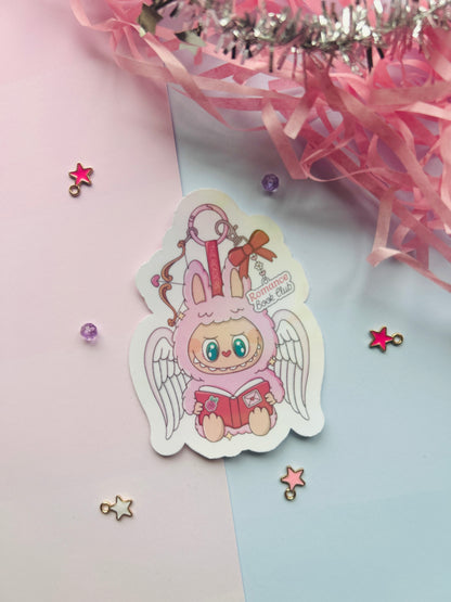 Sticker of a cartoon character with bunny ears and angel wings on a pink and blue background.