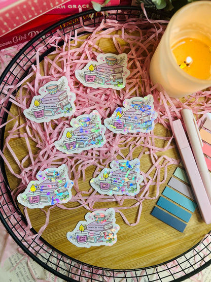 Holographic book stack sticker featuring a tea cup, books labelled with romance tropes (Enemies to Lovers, Slow Burn, Fated Mates), and cosy bookish details.