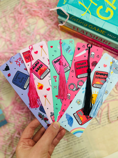 Collection of colorful bookmarks with various designs held by a hand, with books in the background.