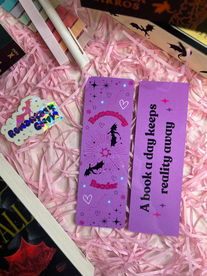 Purple bookmarks with enchanting designs featuring phrases like 'Romantasy Reader' with bats and stars, and 'A book a day keeps reality away,'