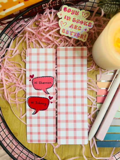 Two pink gingham checked bookmarks inspired by Binding 13 by Chloe Walsh, featuring speech bubbles saying "Hi Shannon" and "Hi Johnny," surrounded by bookish accessories and soft pink aesthetic decor.