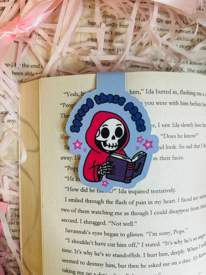 Magnetic bookmark featuring a cute skeleton in a red hoodie reading a book with the phrase 'Spread Those Pages,'