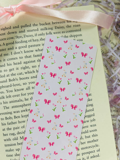 Set of three pastel bookmarks with silly goose and bow designs, placed on an open book with soft pink ribbon, shredded filler, and pens.