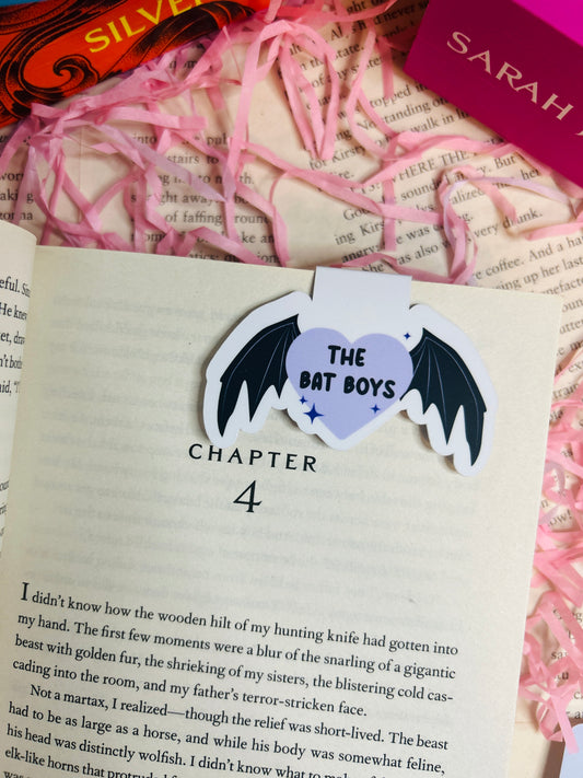 Heart-shaped sticker with bat design on a book page, surrounded by pink ribbons and a book titled 'Silver'.