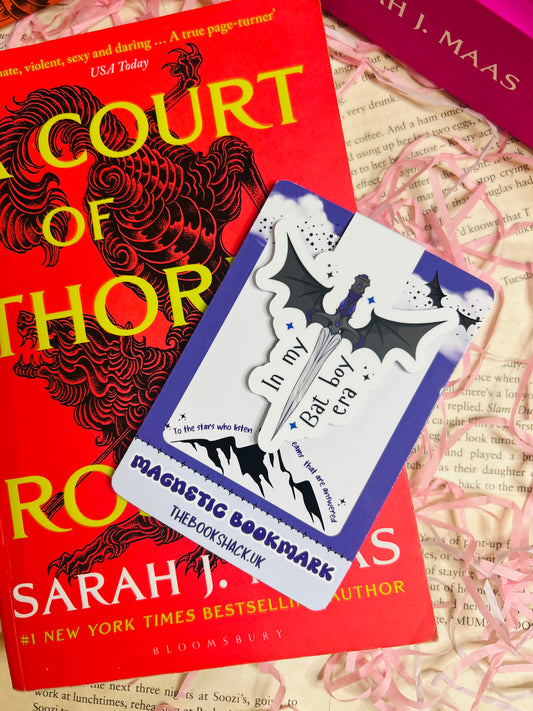 Magnetic bookmark shaped like a sword with bat wings and the phrase "In my Bat Boy era", clipped to an open fantasy book page.