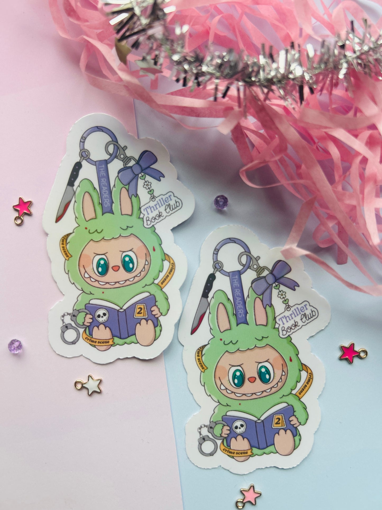 Two stickers of a green character reading a book with decorative elements on a light pink background.